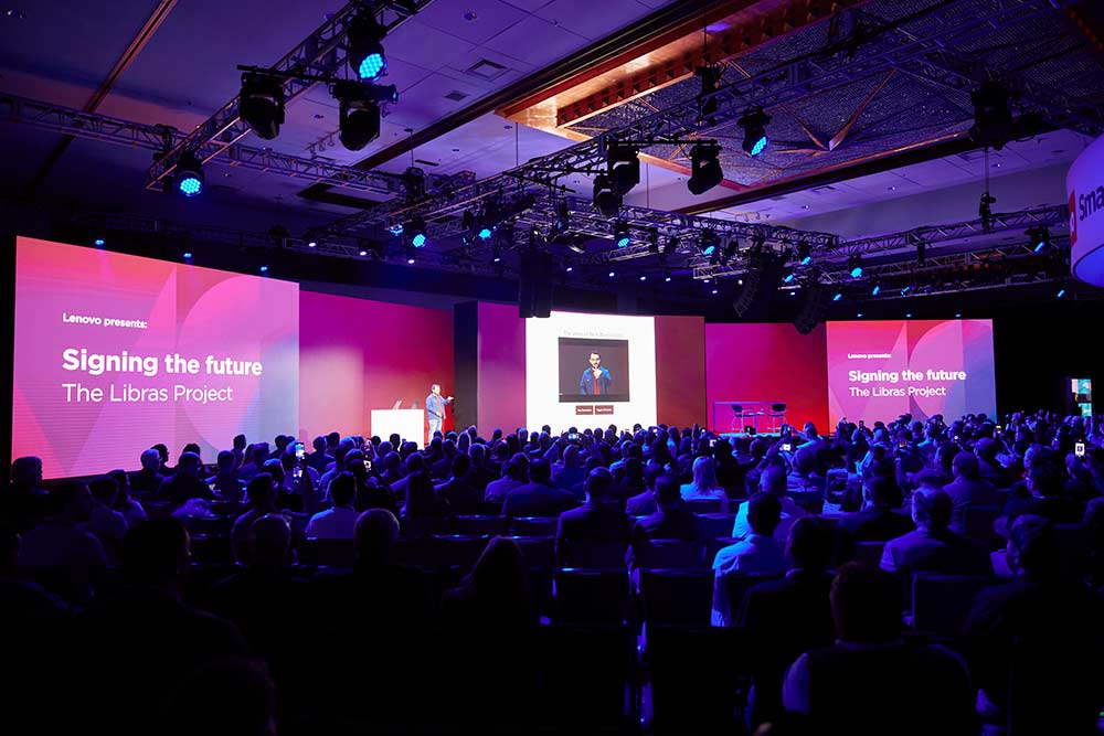 Wide shot the Lenovo TechWorld stage with a speaker and a video presentation