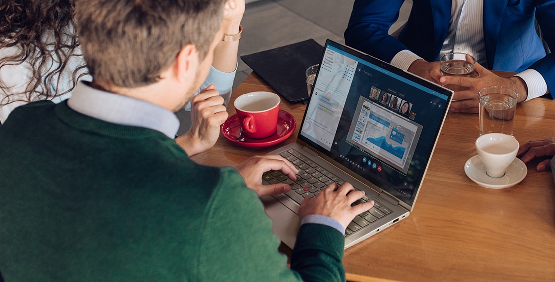 Persone attorno a un tavolo con qualcuno in videoconferenza sul laptop 2 in 1 Lenovo ThinkPad X1 Yoga Gen 7 che mostra display e tastiera.